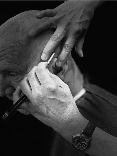 A steady hand drawing a straight razor down a lathered jawline, in black and white.