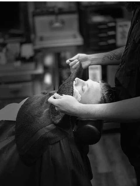 A client reclined in the chair mid-shave, in black and white.