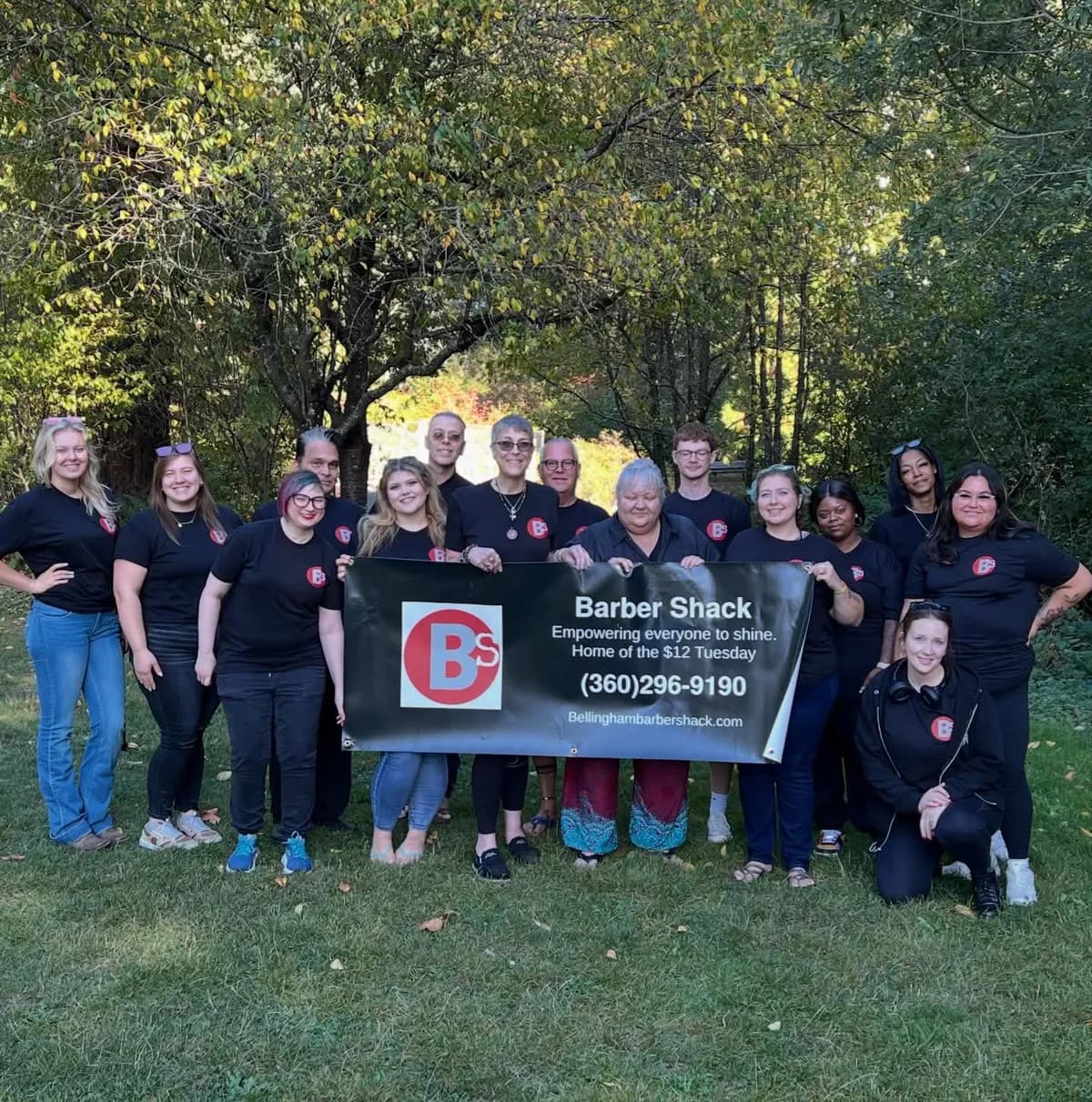 The Barber Shack team holding a banner that reads Empowering everyone to shine, Home of the $12 Tuesday.